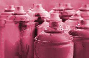 A lot of dirty and used aerosol cans of paint. Macro photograph with shallow depth of field. Selective focus on the spray nozzle Image toned in Viva Magenta, color of the 2023 year photo