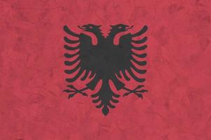 Albania flag depicted in bright paint colors on old relief plastering wall. Textured banner on rough background photo