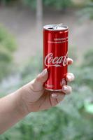 Caucasian woman holds red Coca-Cola tin can with green garden background photo