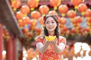 Asian woman in red cheongsam qipao dress is holding ancient gold money inside Chinese Buddhist temple during lunar new year for best wish blessing and good luck concept photo