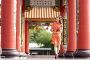 Asian woman in red cheongsam qipao dress holding paper fan while visiting the Chinese Buddhist temple during lunar new year for traditional culture concept photo