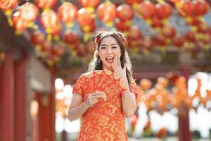 Asian woman in red cheongsam qipao dress is holding red envelope for money saying 'May you have great luck and profit' inside Chinese Buddhist temple during lunar new year for best wish blessing photo