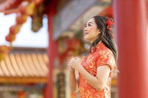 Asian woman in red cheongsam qipao dress is making a wish to ancestral god inside Chinese Buddhist temple during lunar new year for  for best wish blessing and good luck concept photo