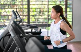 joven atleta asiática feliz correr en cinta rodante, máquina de correr, en gimnasio interior fitness para la salud foto