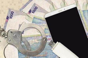 1000 Indonesian rupiah bills and smartphone with police handcuffs. Concept of hackers phishing attacks, illegal scam or malware soft distribution photo