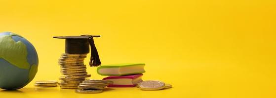 Banner with graduated cap with coins and globe on yellow background. Savings for education concept photo