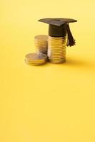 Graduated cap with coins on yellow background. Savings for education concept photo