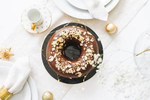 Large round chocolate almond cake on the table with New Year serving, christmas white scandinavian festive table, top view, winter flat lay photo