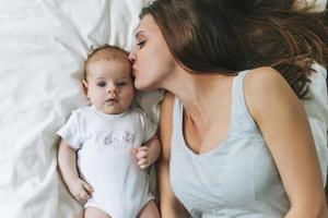 Young mother having fun with cute baby girl on the bed, natural tones, love emotion photo