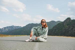 Beautiful smiling young woman traveler in casual clothes on road, trip to mountains photo