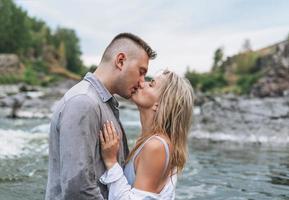 feliz pareja joven enamorada de los viajeros besándose en el río de la montaña foto