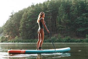The slim young woman in green sweemsuit on sup boat with oar floating on the river, weekend trip and local travel photo