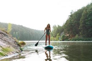 la joven delgada con traje de baño verde en un bote con remo flotando en el río, un viaje de fin de semana y un viaje local foto