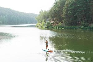 The slim young woman in green sweemsuit on sup boat with oar floating on river, weekend trip and local travel photo