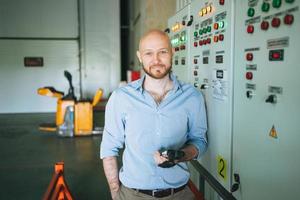 adulto calvo sonriente hombre atractivo cuarenta años con barba en camisa azul hombre de negocios. ingeniero cerca del gabinete de control del equipo de refrigeración en el almacén foto