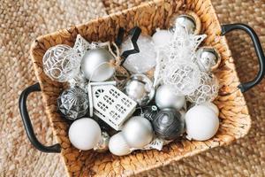 Wicker basket with white and silver Christmas tree toys and balls on floor, top view photo