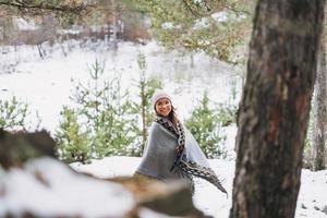 Portrait of young brunette beautiful woman in hat and grey poncho in the winter forest photo