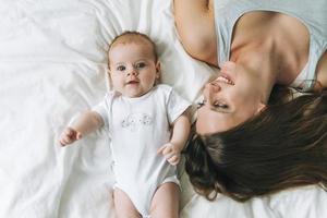 Young mother having fun with cute baby girl on bed with white linen, natural tones, love emotion photo