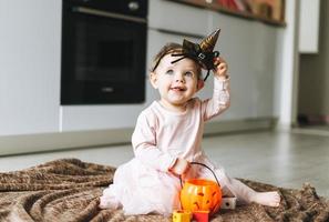 Cute little baby girl in pink dress with the witch's hat and pumpkin lantern sitting on floor in kitchen at the home, Halloween time photo