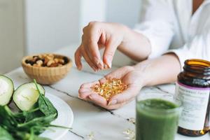 mujer con camisa blanca con omega 3, cápsulas de vitamina d con comida vegana verde. el médico prescribe una receta de medicamentos y vitaminas en la clínica, alimentos saludables y tratamiento foto