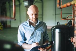 Adult bald smiling attractive man forty years with beard in blue shirt businessman. Engineer near the control cabinet of refrigeration equipment in warehouse photo