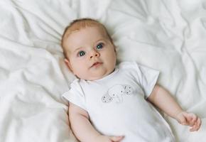 Cute baby girl 2-4 month on bed with white linen, natural tones, selective focus photo