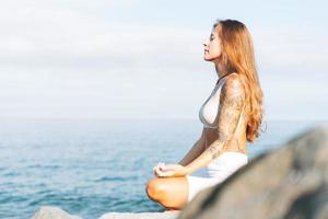 Young fit beautiful woman with long hair in white sport clothes practice yoga and enjoy life on the sea beach, mental and phisical health photo