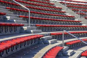 Empty red plastic chairs in the stands of the stadium or amphitheater. Many empty seats for spectators in the stands. photo