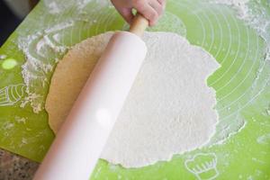 hands knead the dough homemade pastry for bread or pizza Bakery background - child hands prepares the dough and rolling pin with flour on board photo