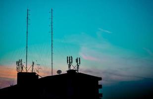 silueta de edificios en la casa con vista al atardecer y torre de radio de comunicación en el cielo azul