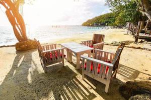 mesa de madera puesta en la playa vista de las olas del mar y el paisaje de la costa - paisaje marino con mesa y silla isla tropical con fondo de cielo azul océano en el resort vacaciones de verano en la playa de tailandia foto