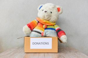 caja de donaciones con fondo de mesa de madera de muñeca de oso de peluche - donar concepto de juguete foto