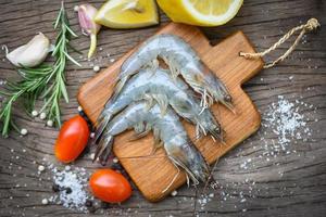 camarones frescos en tabla de cortar de madera con ingredientes hierbas y especias para cocinar mariscos - camarones langostinos crudos foto