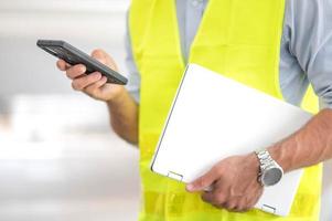 Male hand holding smartphone for check situatiob obout the work and the other hand holding laptop prepare to work at the construction site in the city. photo