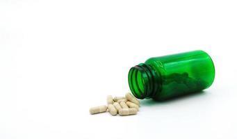 White pills spilling or pour out of green pill bottle isolated on white background with copy space for add text. Healthy, herb, container object and Medicine. Food supplement for cure or repair health photo