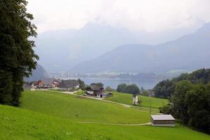 viaje a sankt-wolfgang, austria. la vista sobre el prado verde con las casas, un lago y las montañas al fondo.