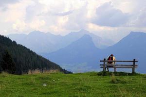 viaje a sankt-wolfgang, austria. el joven está sentado en un banco con vistas a las montañas. foto