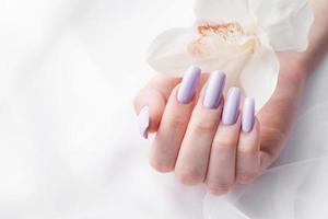 Girl's hands with delicate purple manicure and orchid flowers photo