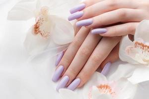 manos de niña con delicada manicura púrpura y flores de orquídeas