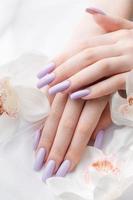 manos de niña con delicada manicura púrpura y flores de orquídeas foto