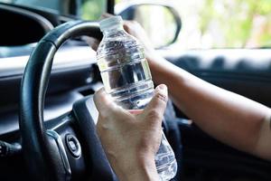 Asian woman driver hold cold water for drink in car, dangerous and risk an accident. photo