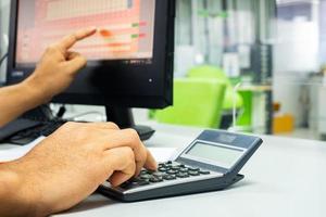 la mano del hombre está usando la calculadora para informar el trabajo en la computadora, para presentar el informe de ganancias comerciales, el concepto de negocios y finanzas. foto