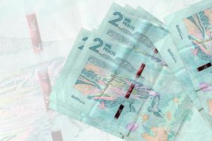 Los billetes de 2 pesos colombianos se encuentran apilados sobre el fondo de un gran billete semitransparente. presentación abstracta de la moneda nacional foto