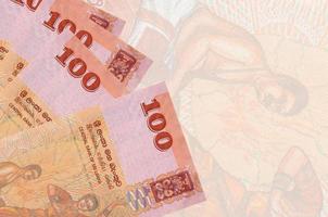 100 Sri Lankan rupees bills lies in stack on background of big semi-transparent banknote. Abstract business background photo