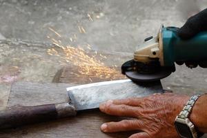 Closeup hands are sharpening a knife with electric sharpener grinder machine in motion action of sparking. Concept, traditional style of fixing tool. photo