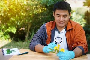 un apuesto profesor de ciencias asiático sostiene una lupa para inspeccionar las flores. concepto, enseñanza y aprendizaje al aire libre. asignatura de ciencias, trabajo de proyecto. experimento, educación, aprender haciendo enfoque. foto