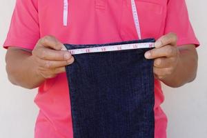 Closeup tailor uses measuring tape to measure width of jeans leg. Concept, DIY, sewing. Handcraft. Tailor, Repair clothing at home. Check size. prepare to cut shorten the jeans. photo