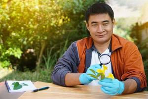 un apuesto profesor de ciencias asiático sostiene una lupa para inspeccionar las flores. concepto, enseñanza y aprendizaje al aire libre. asignatura de ciencias, trabajo de proyecto. experimento, educación, aprender haciendo enfoque. foto