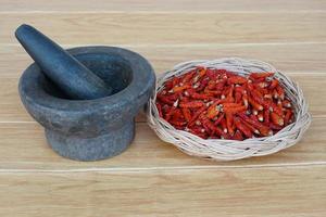 viejo mortero de piedra de granito con mortero y canasta de chiles rojos secos para cocinar. concepto, utensilios de cocina. herramienta de cocina tailandesa, uso para machacar pasta de chile o pasta de curry. foto