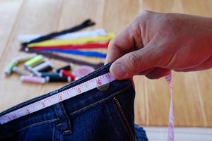 Closeup tailor hand use measuring tape to measure width of jeans waist. Concept, DIY, sewing. Handcraft. Design ,fix or repair of cutting clothes. photo